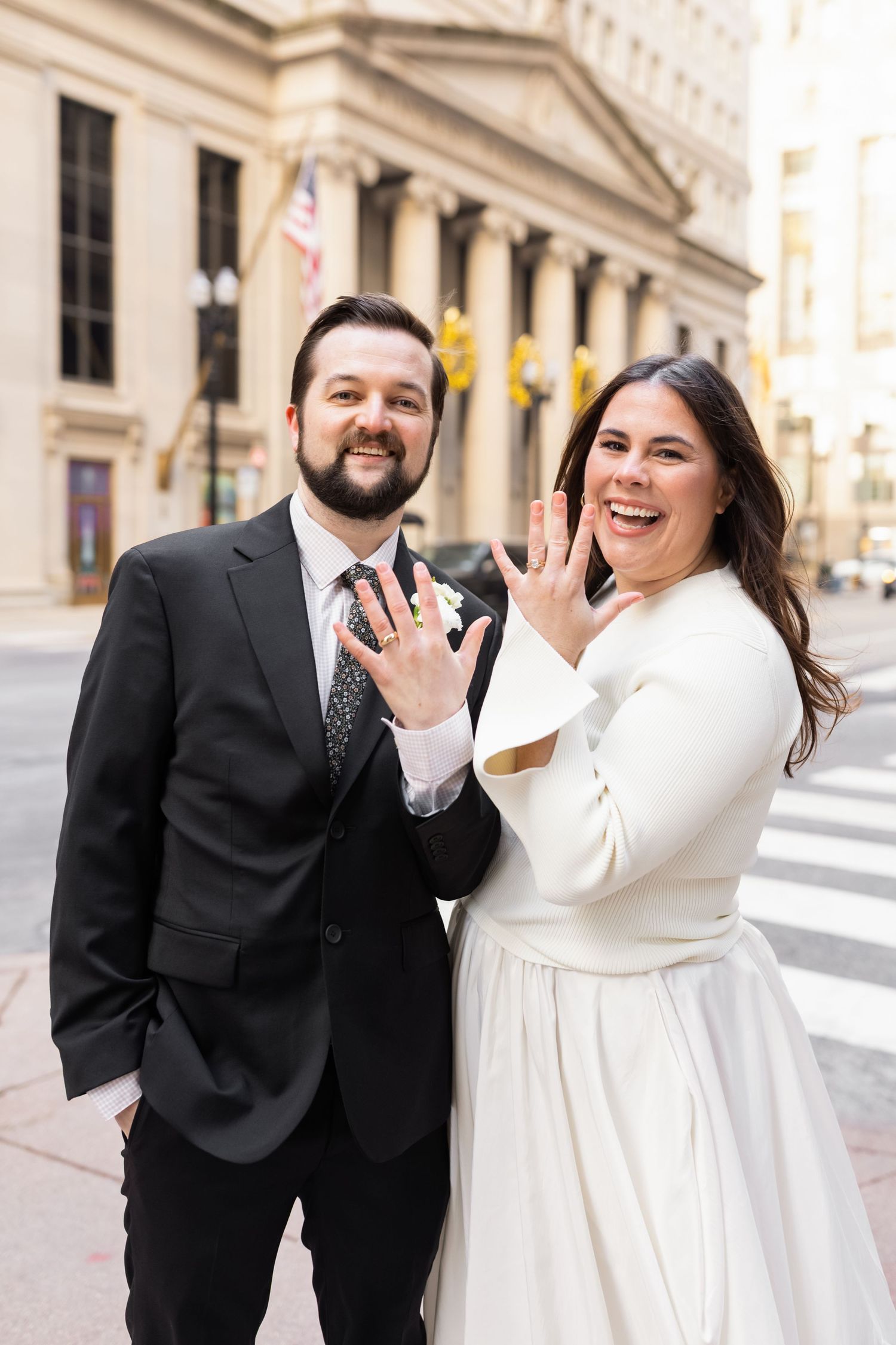 Joyful newlyweds show off their wedding rings to the camera on a Chicago city street after elopement.