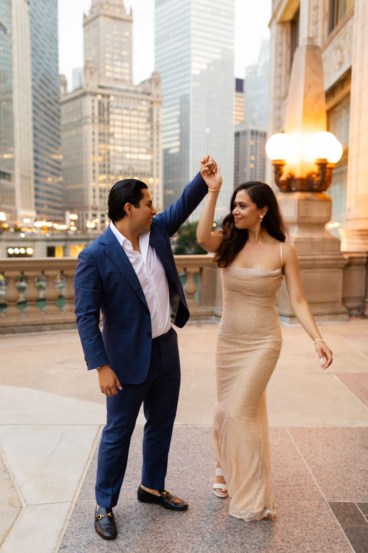 Couple dancing on Chicago city street, man in blue suit twirling woman in gold gown with skyscrapers behind.