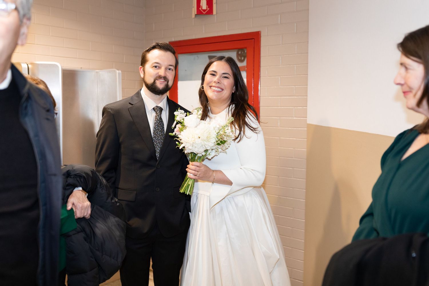 Bride and groom smile warmly while waiting inside Chicago City Hall with guests on their wedding day.