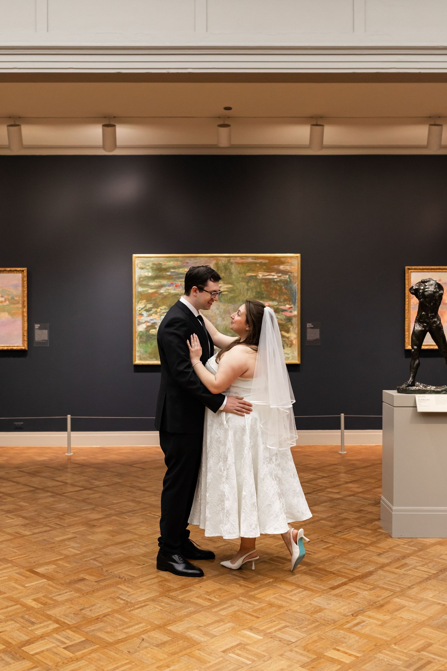 Bride and groom dancing in art museum gallery surrounded by Monet paintings on their wedding day.