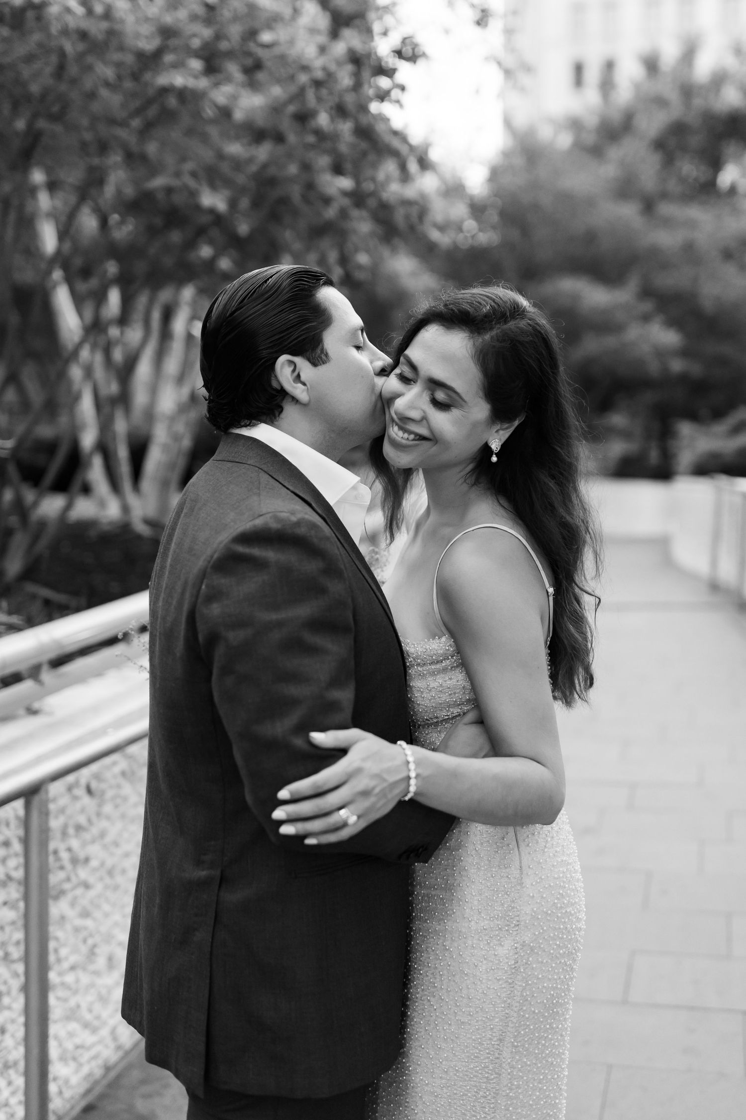 Black and white photo of man kissing woman's cheek during romantic outdoor engagement session.