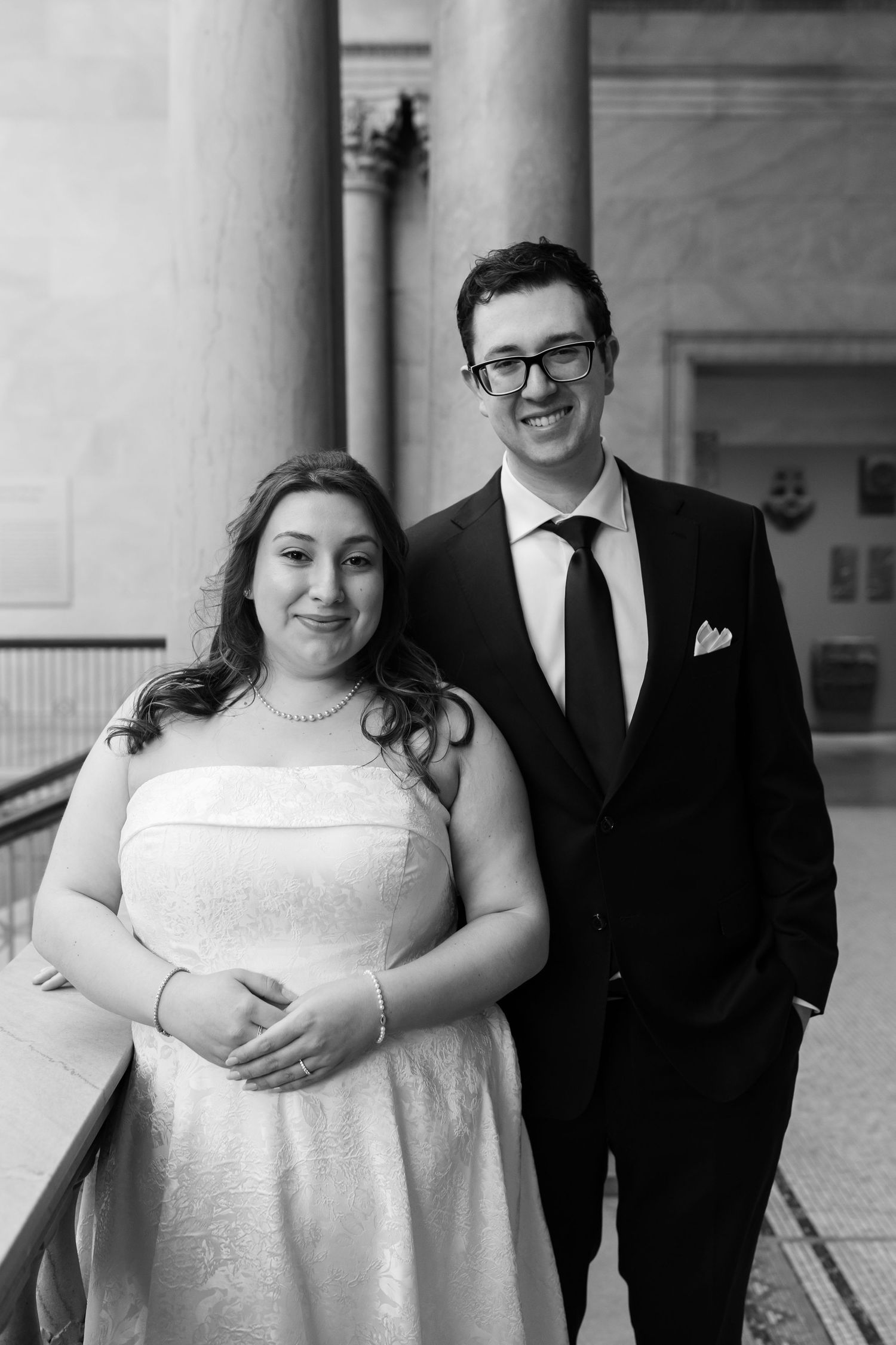 Black and white portrait of smiling bride and groom standing together near stone columns.