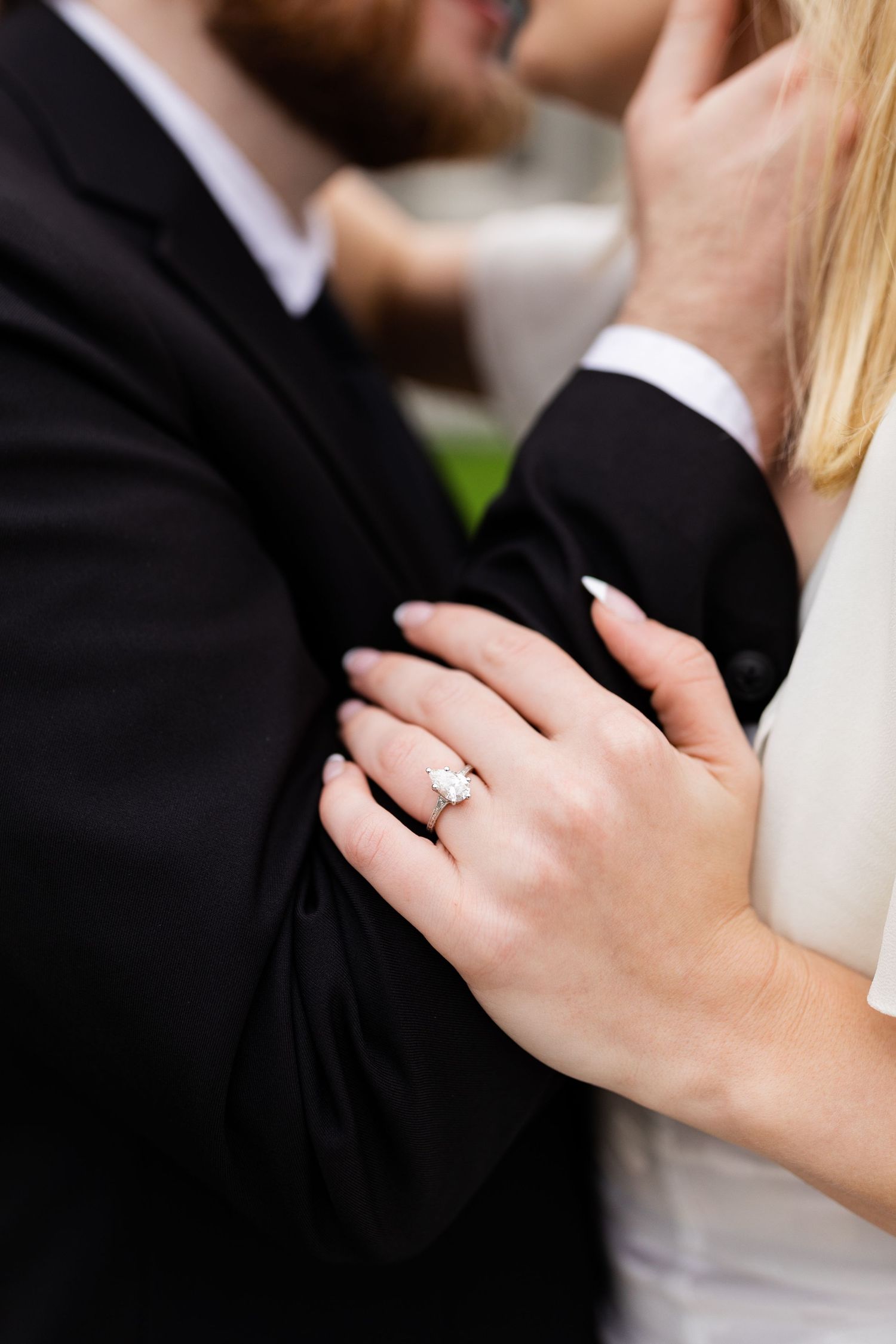 Close-up of bride's elegant diamond engagement ring as couple embraces during wedding photos.