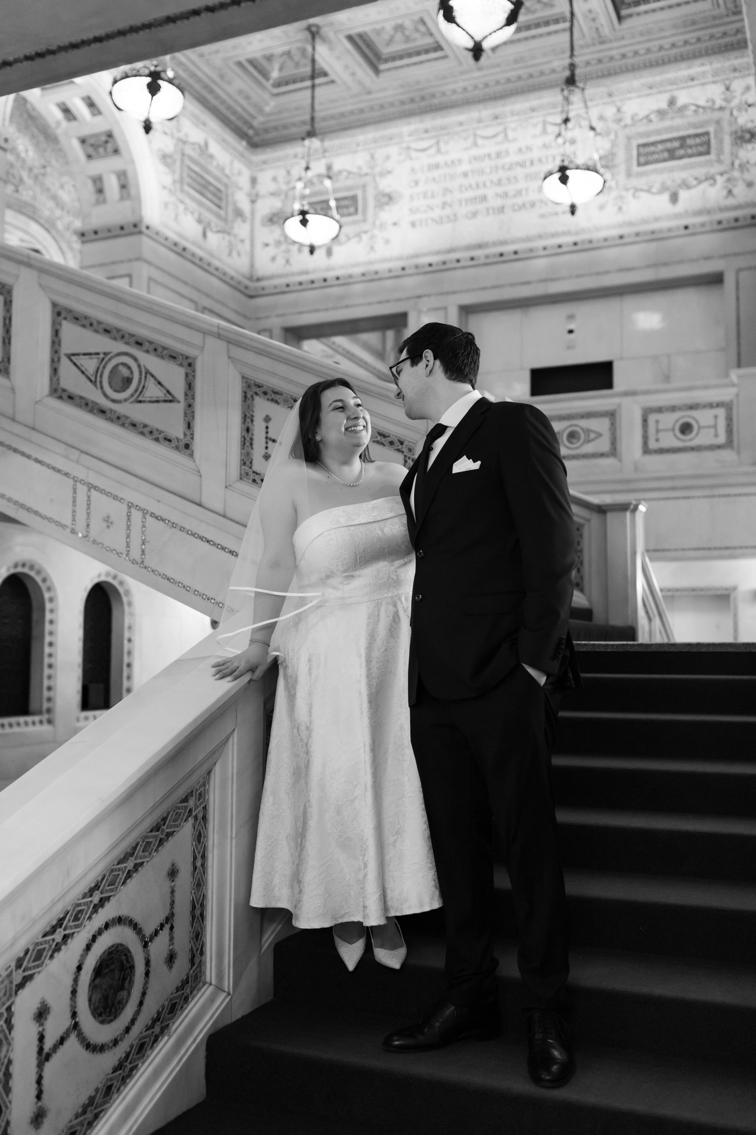 Black and white photo of bride and groom sharing a romantic moment on grand ornate staircase.