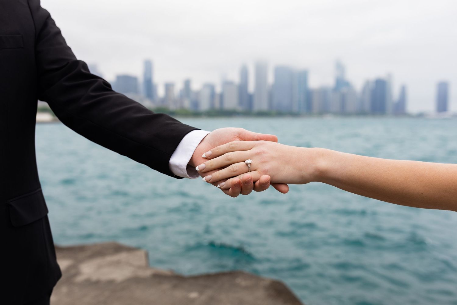 Bride and groom hold hands near Lake Michigan with the Chicago city skyline behind them.
