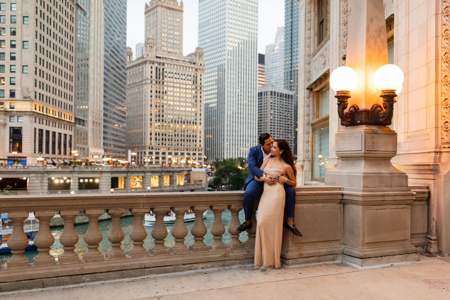 Elegant couple posing by stone balustrade on Chicago Riverwalk with stunning downtown skyline at sunset.