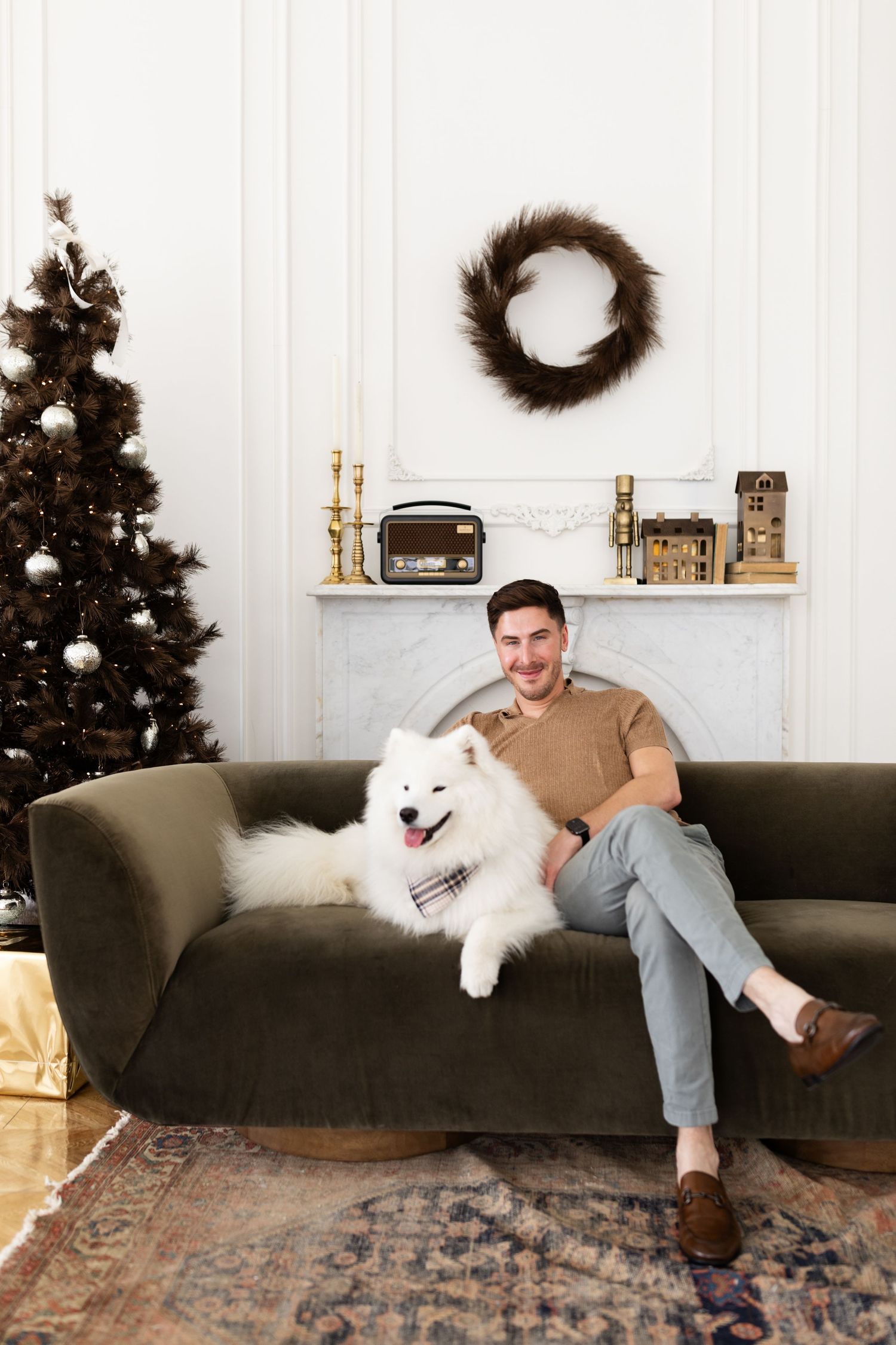 Man relaxing on green velvet sofa with white Samoyed dog in elegant Christmas holiday decorated interior.