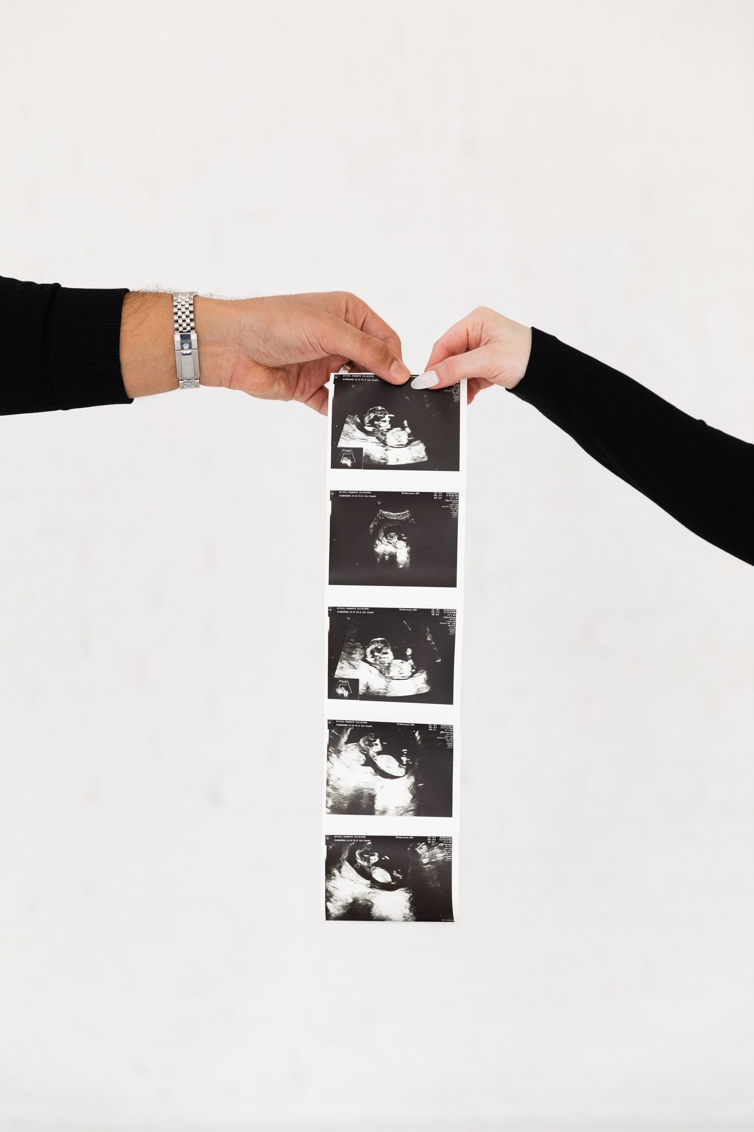 Expecting couple holding ultrasound photo strip together against white background.