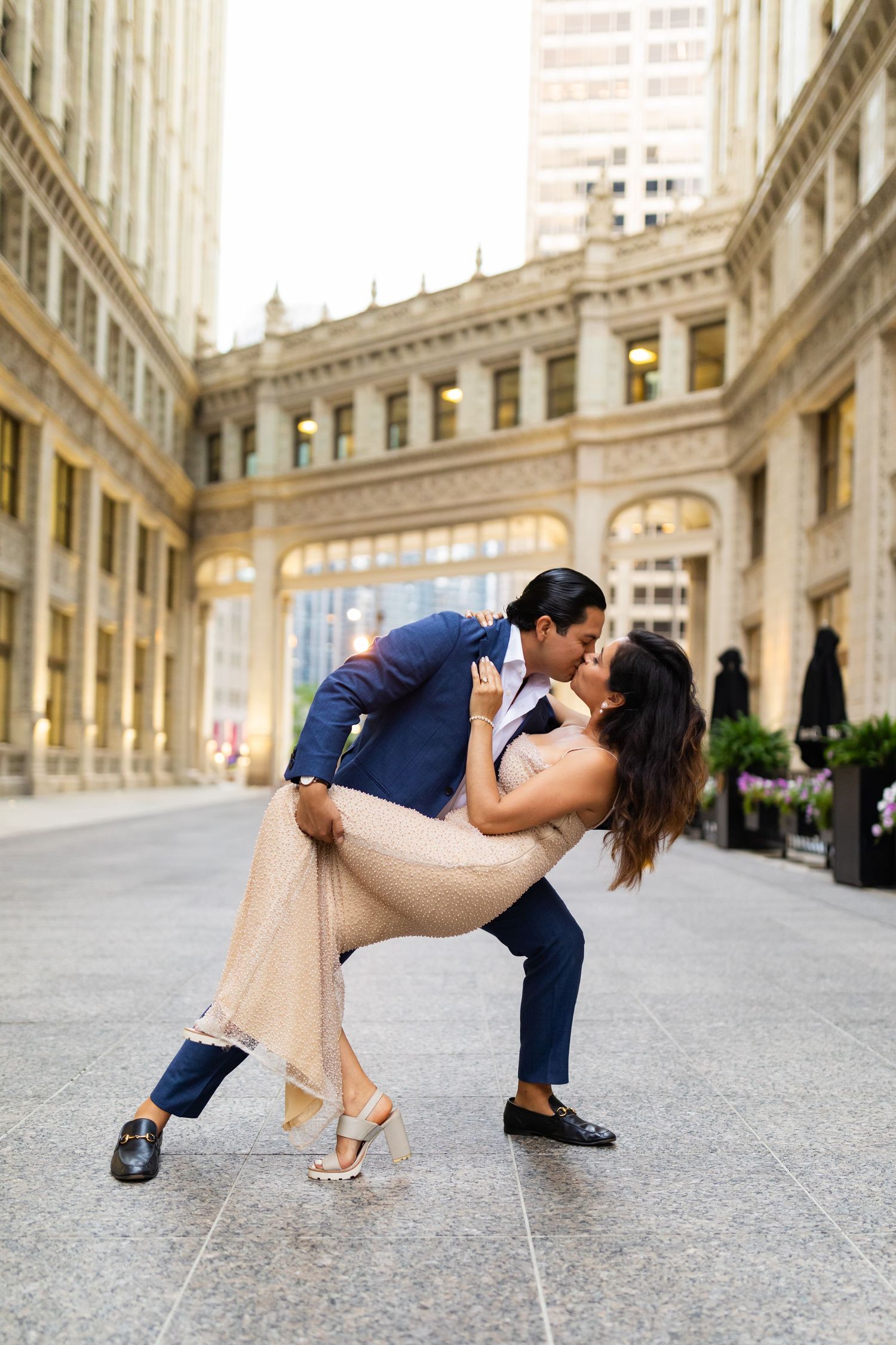Couple shares romantic dip kiss in front of historic Chicago building during elegant engagement photo session.
