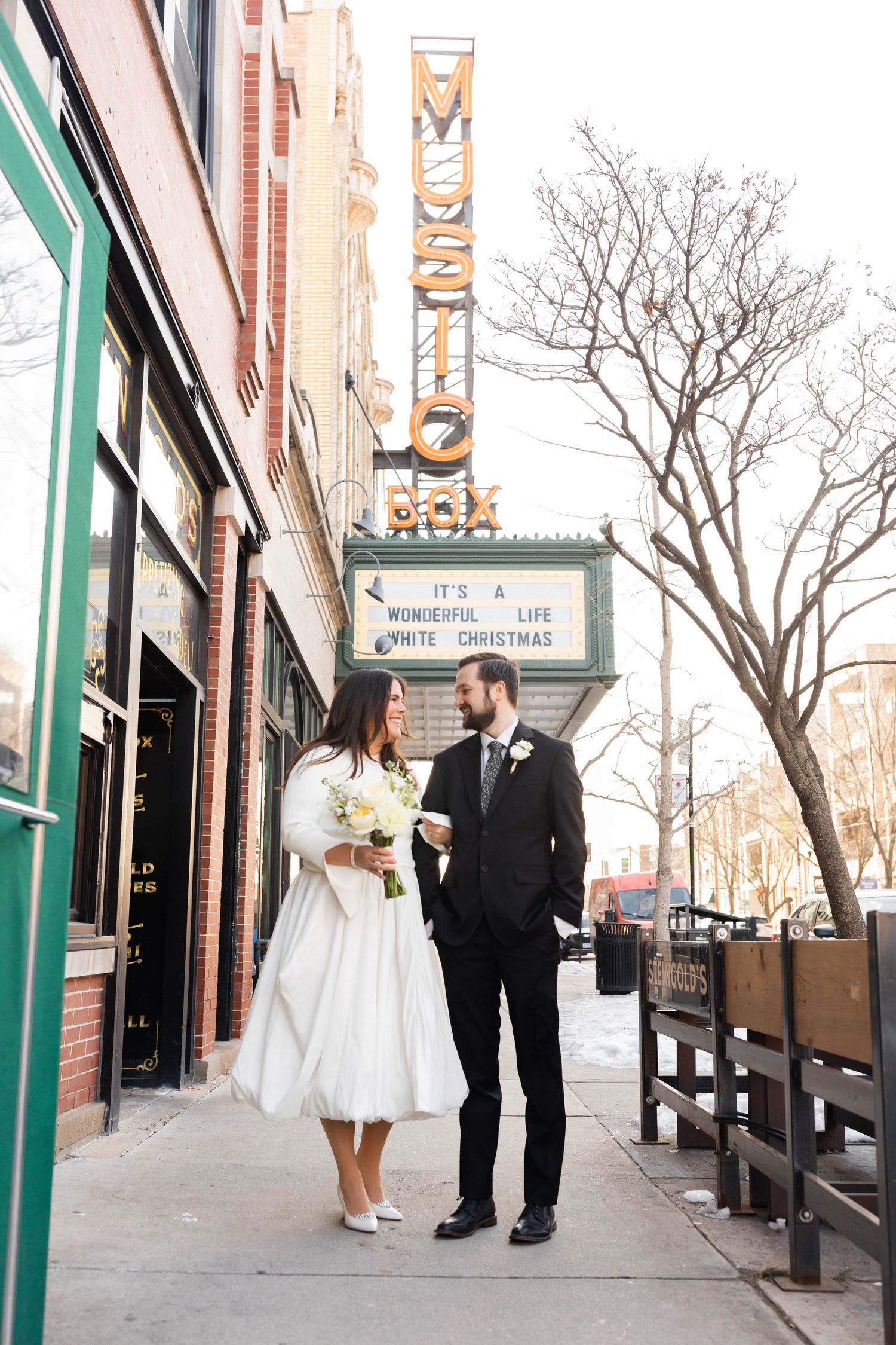 Bride and groom posing on sidewalk in front of the Music Box Theatre marquee in winter.