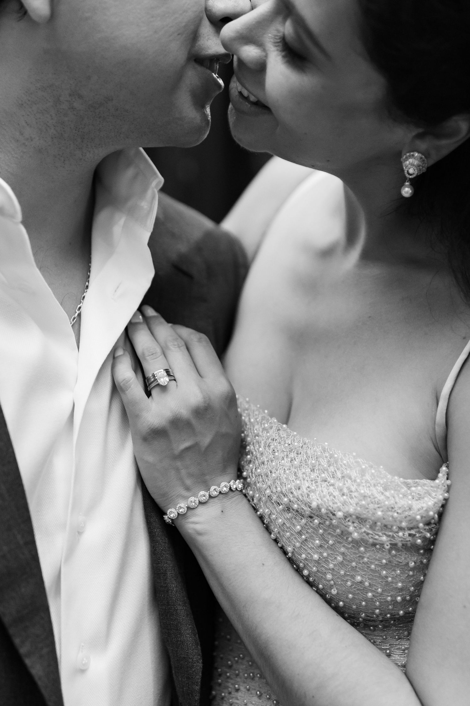 Black and white close-up of couple almost kissing, woman's hand showing diamond ring and pearl bracelet.
