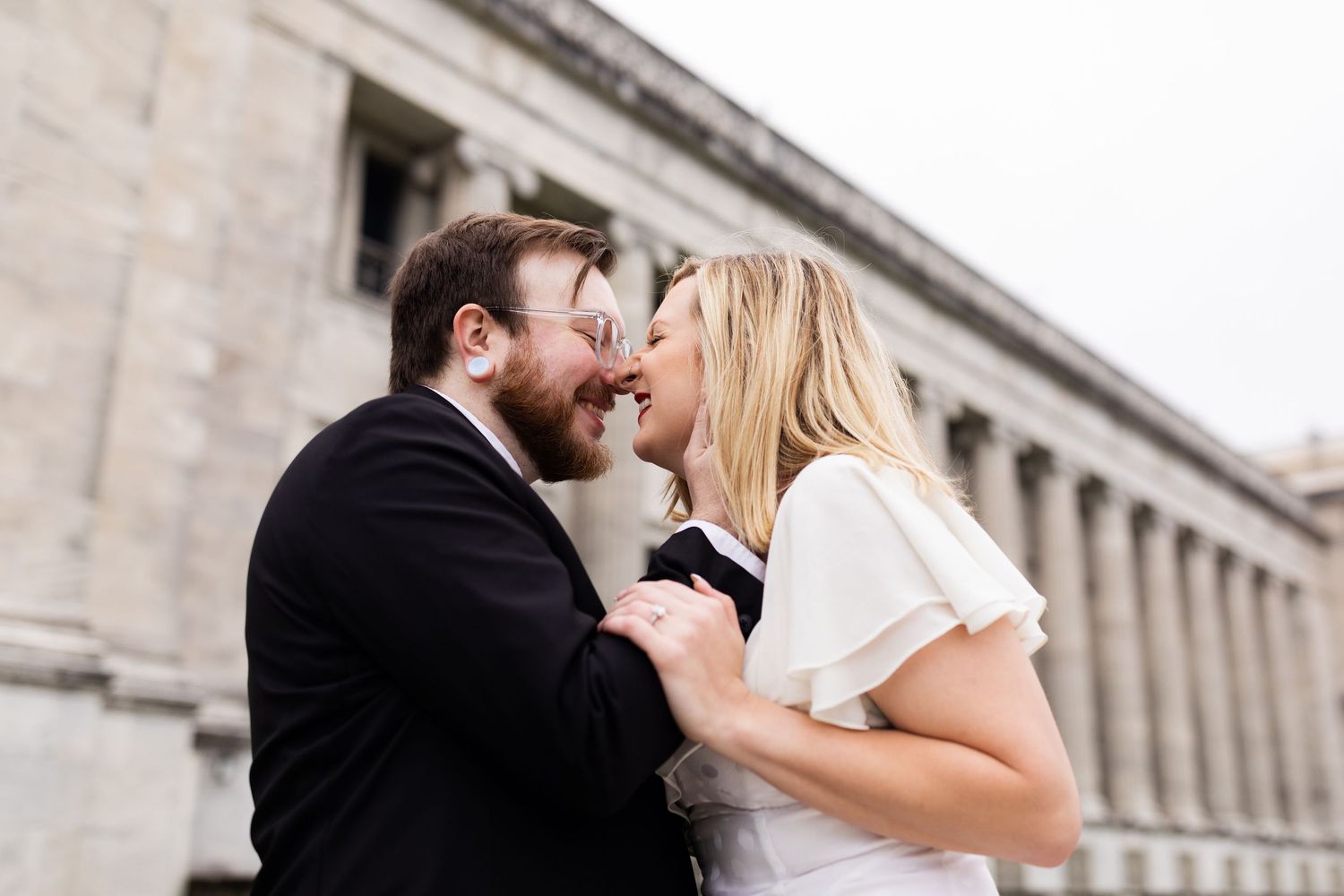 Bride and groom laugh together outside a historic columned building during engagement photos.