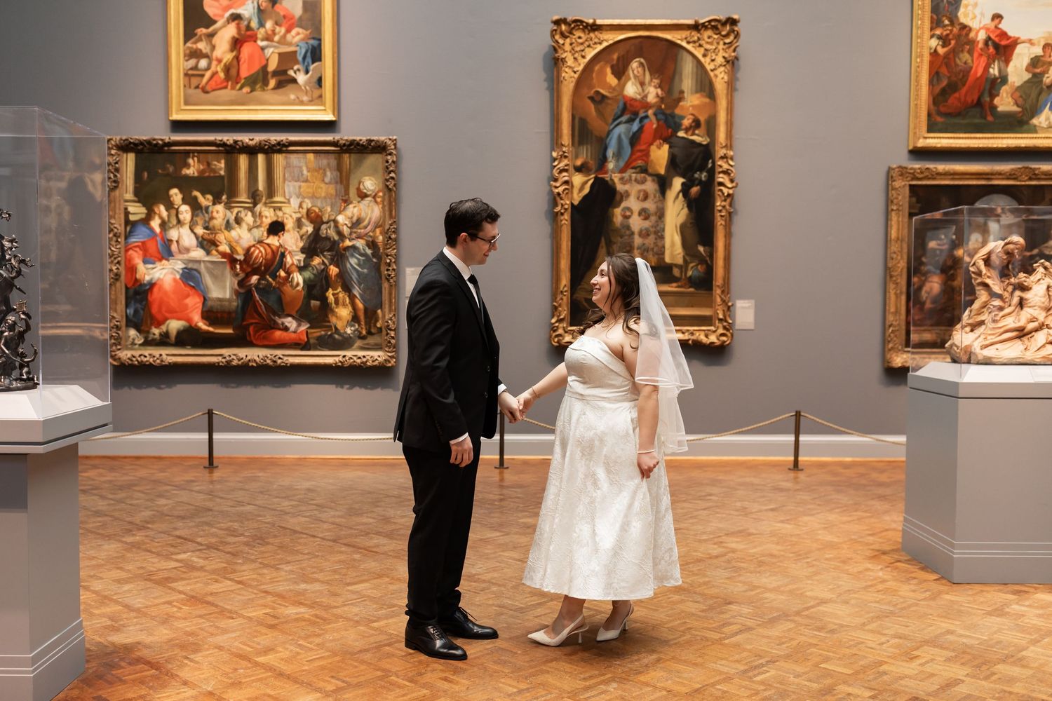 Newlywed couple dances playfully through elegant art museum gallery filled with classical paintings.