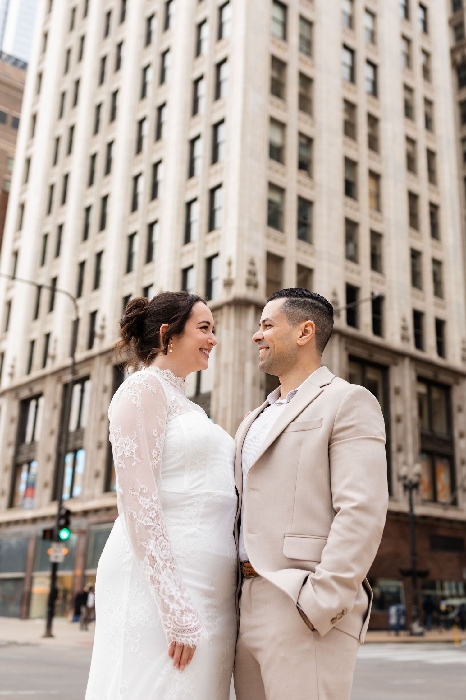 Bride and groom gazing at each other lovingly on a city street with a tall historic building behind them.