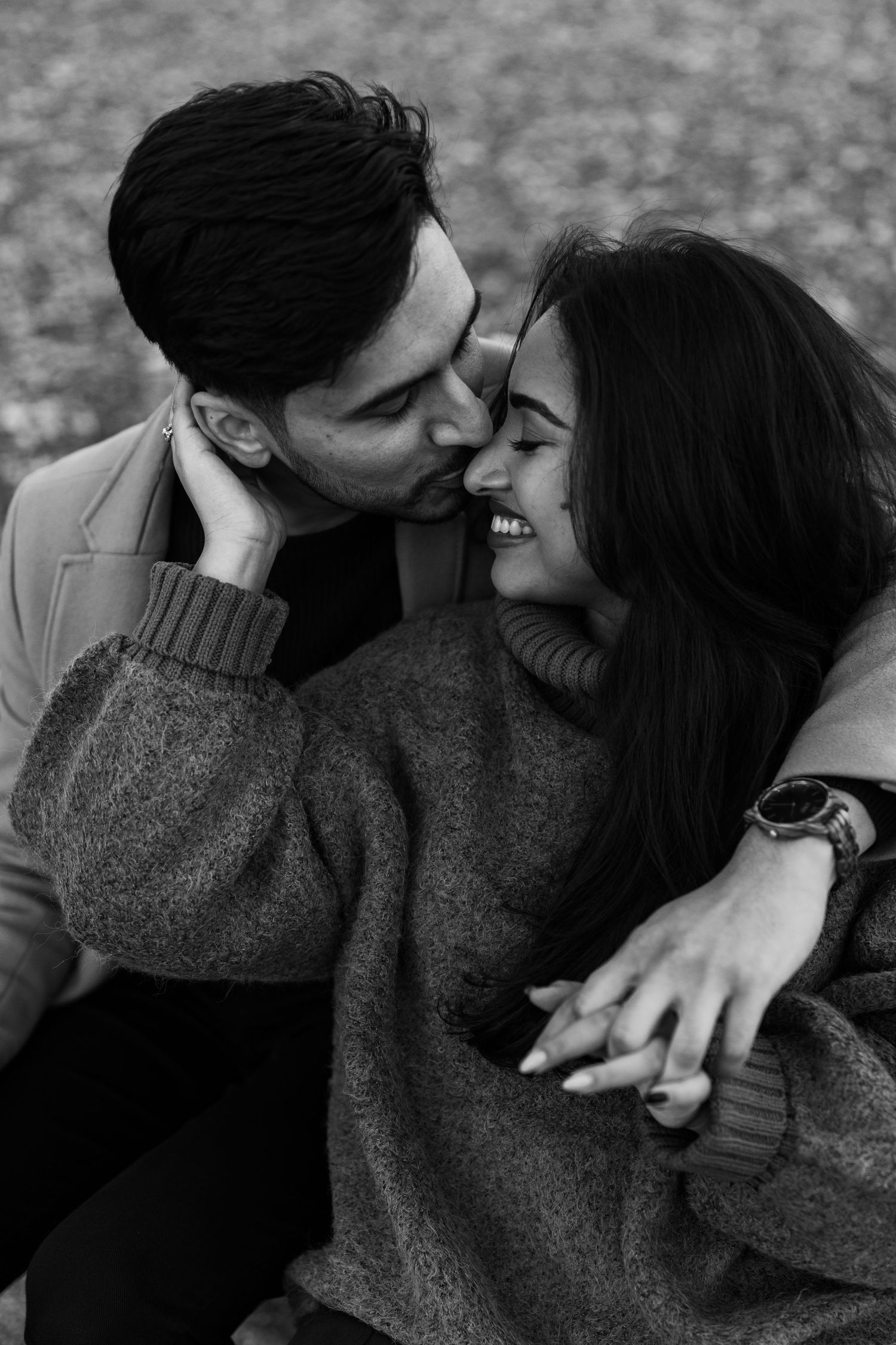 Black and white close-up of couple embracing, man kissing woman's cheek, both smiling tenderly, woman wearing watch.