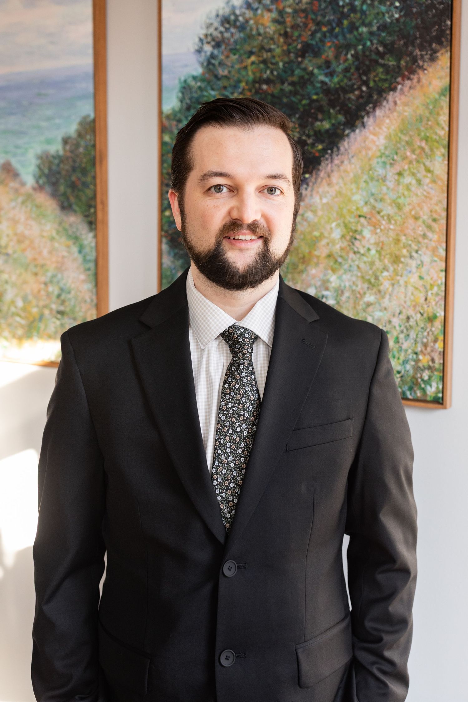 Smiling groom in black suit and patterned tie poses before colorful impressionist painting.
