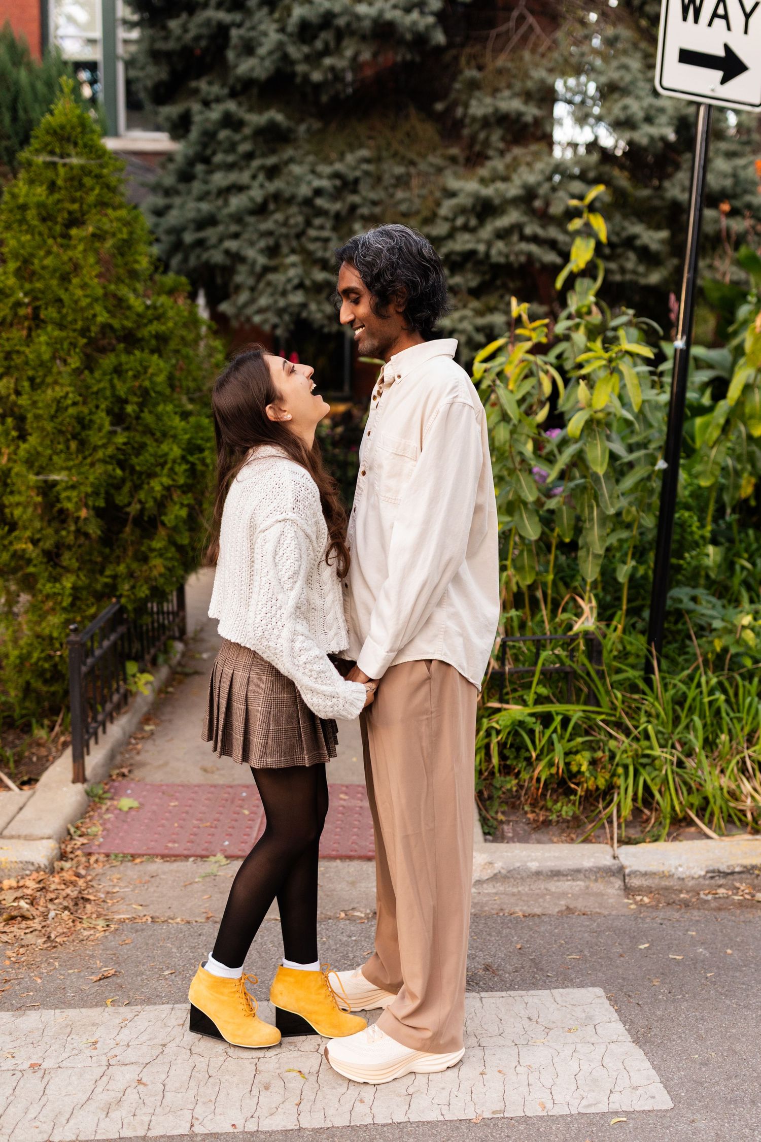Interracial couple holding hands and facing each other on urban crosswalk near one-way street sign.