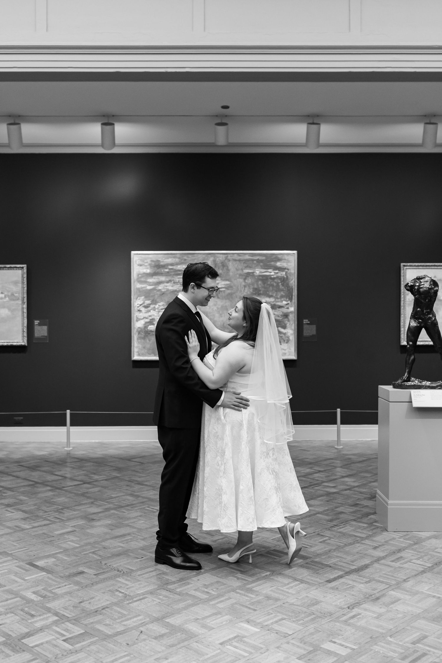 Black and white photo of bride and groom dancing in an art museum gallery on their wedding day.