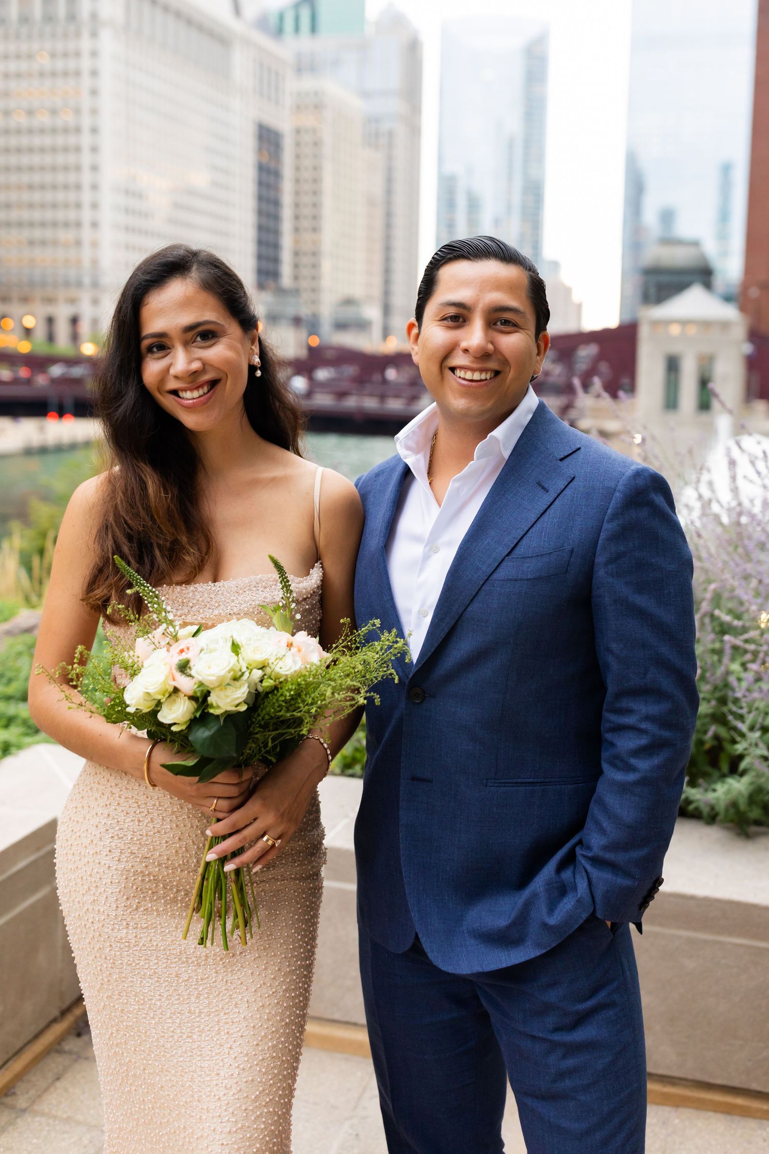Elegant couple posing with white floral bouquet along Chicago Riverwalk with city skyline backdrop.