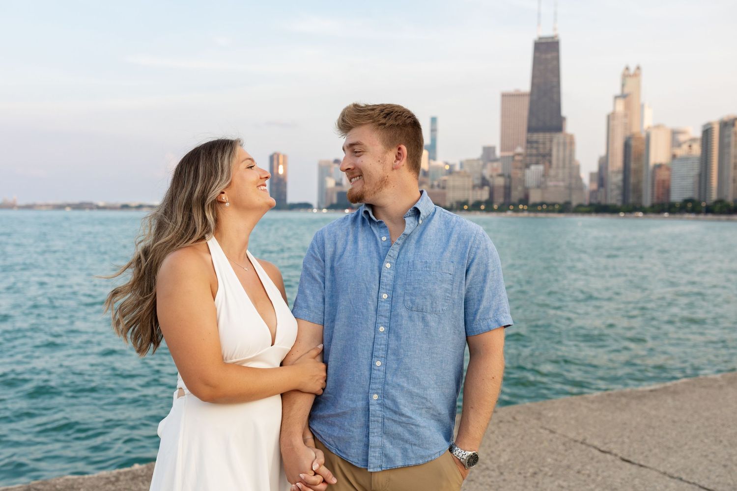 Happy couple holding hands and laughing together on a lakefront with Chicago skyline in the background.