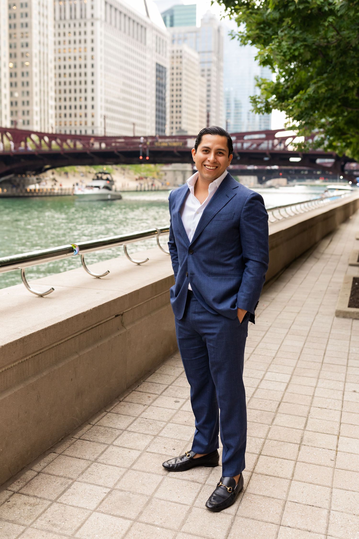 Groom in navy blue suit smiling confidently while standing along the Chicago Riverwalk on wedding day.