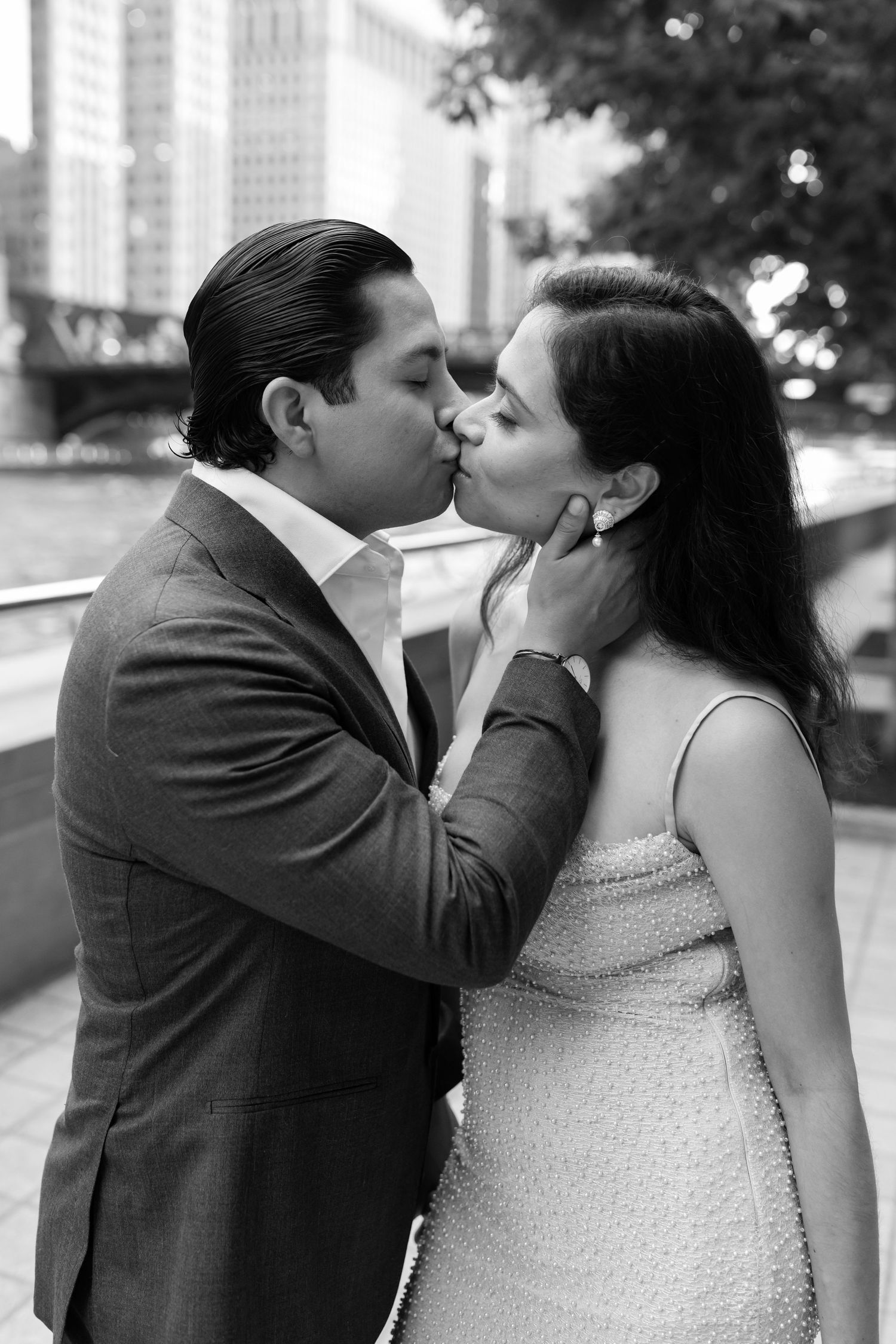 Black and white romantic photo of groom kissing bride tenderly on the cheek near Chicago River.