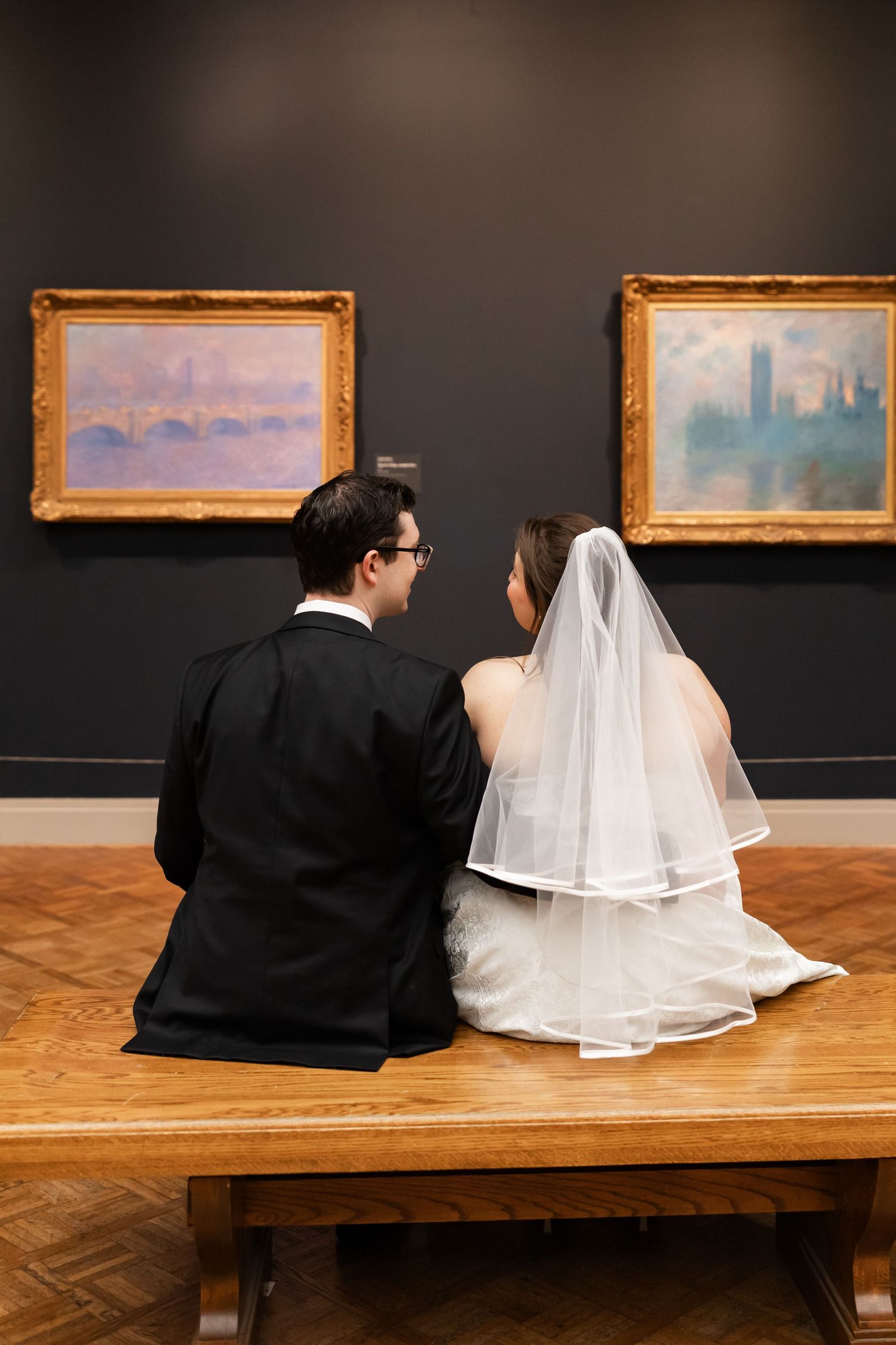 Newlywed couple sitting on a museum bench viewing Monet paintings during their wedding photo session.