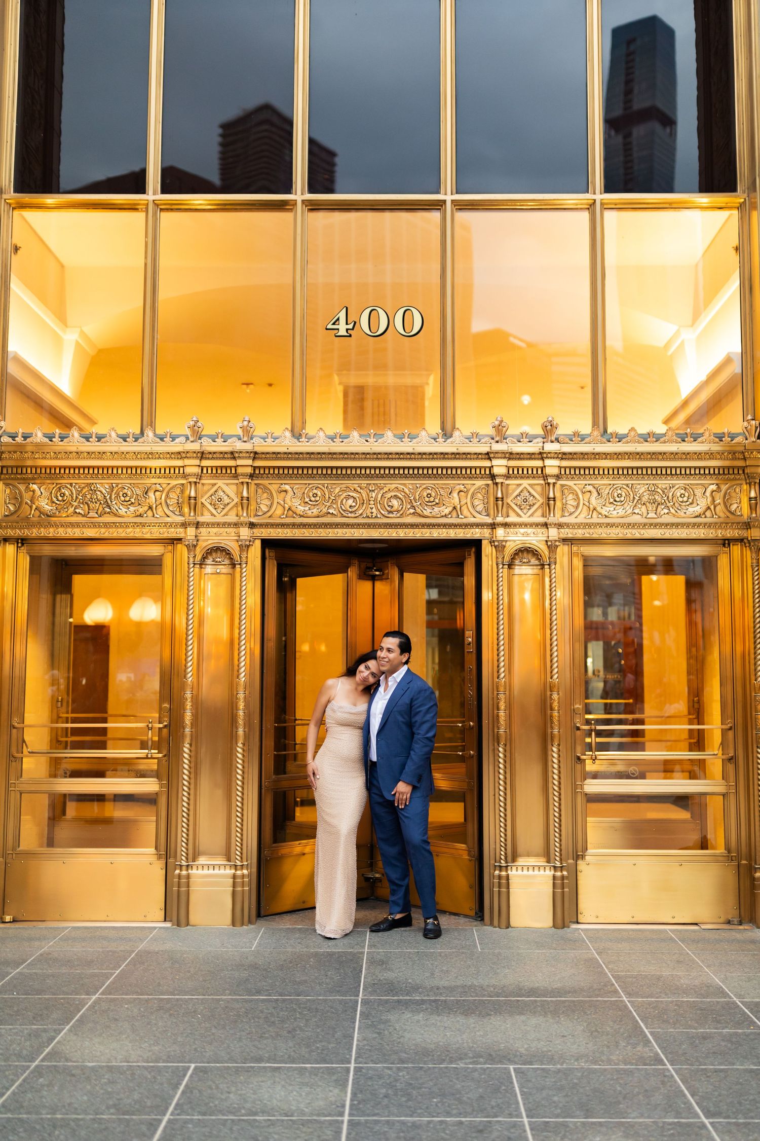 Couple embracing before glowing gold entrance of 400 building during evening engagement photoshoot.