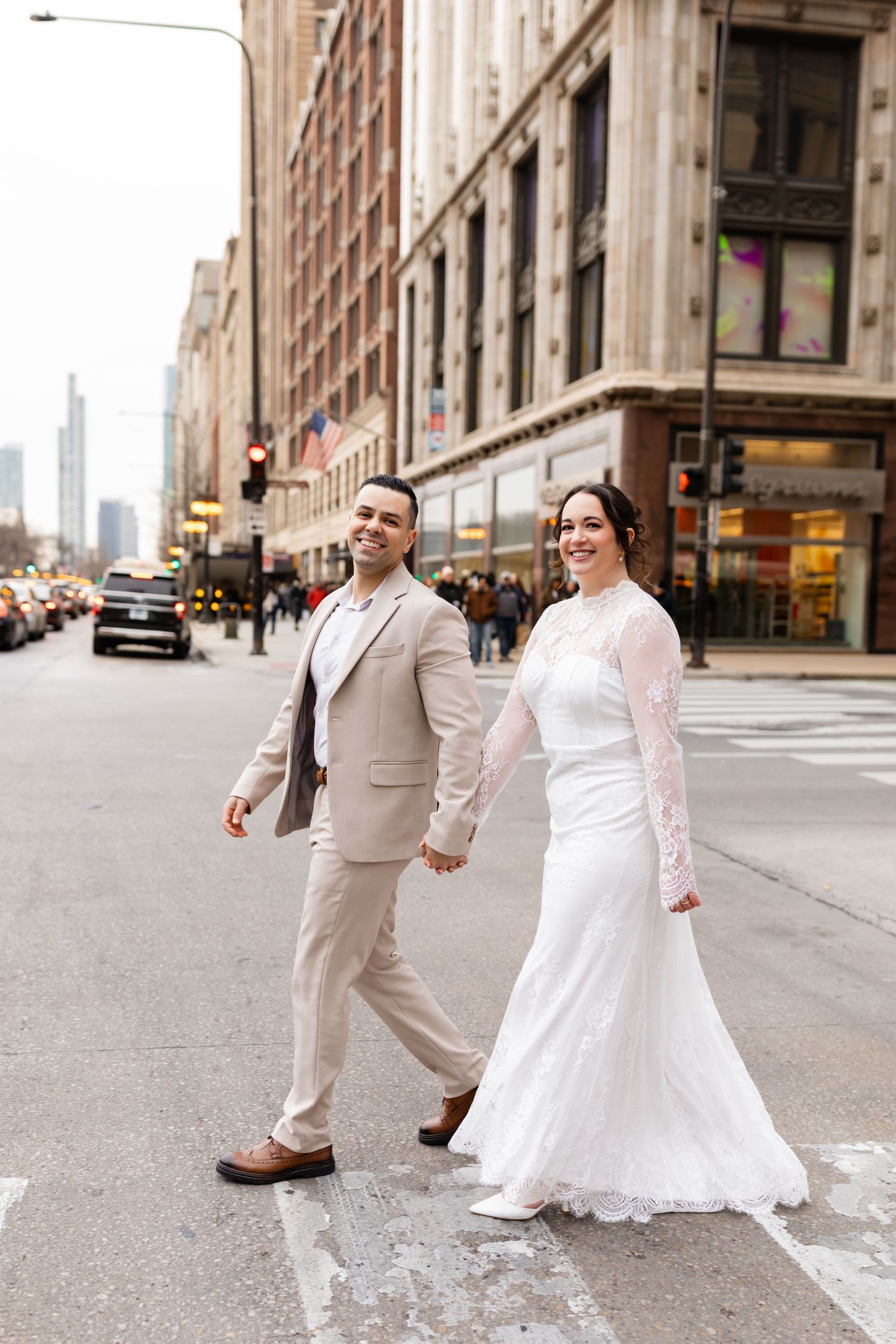 Smiling bride and groom hold hands while crossing a busy city street in downtown Chicago.