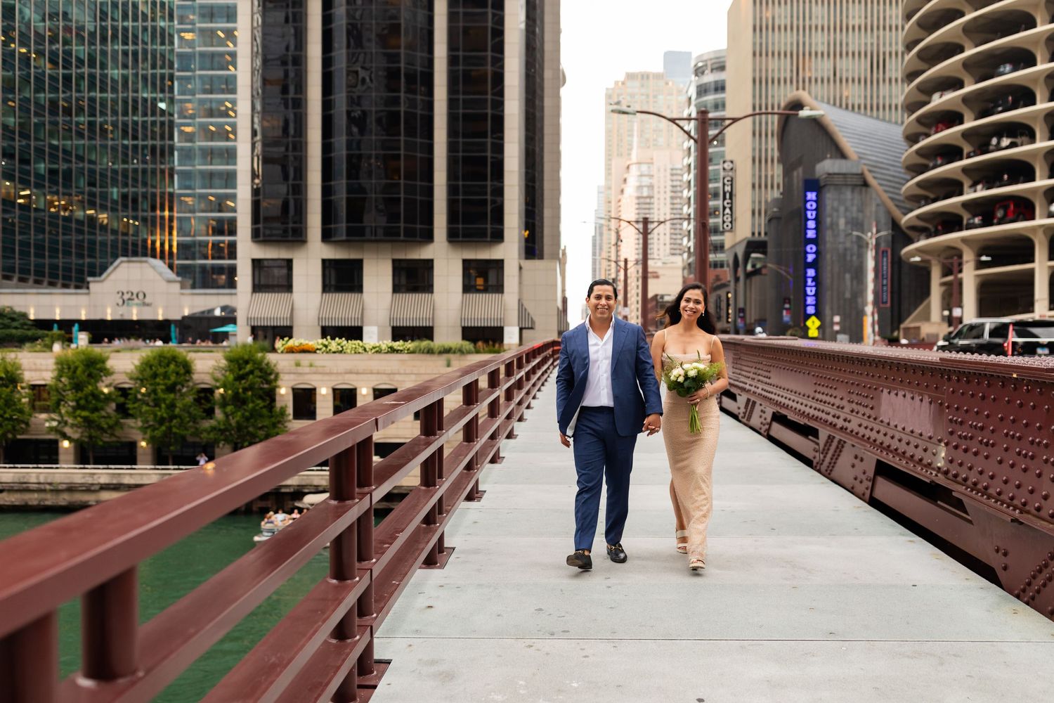 Bride and groom walking hand in hand across a Chicago bridge with urban skyline in background.