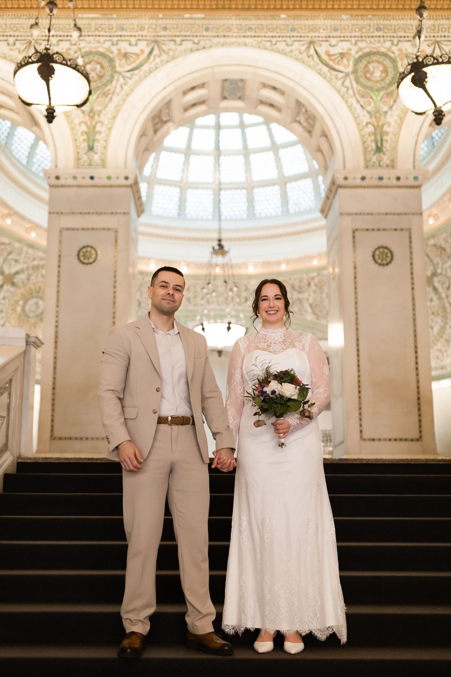 Bride and groom posing together on grand staircase inside beautifully decorated historic Chicago building.