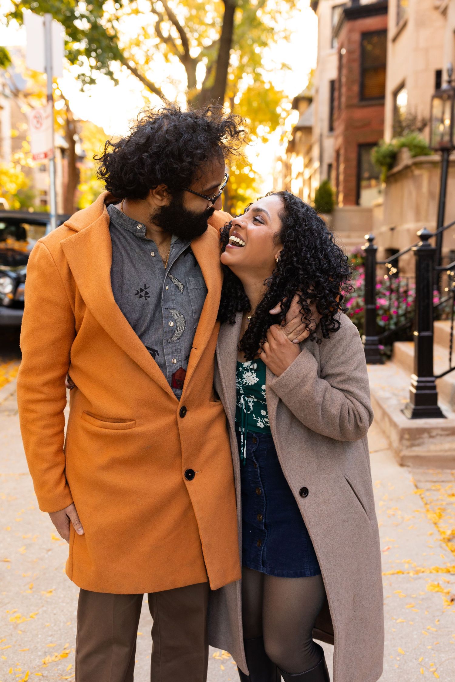 A laughing couple shares a joyful moment on a city sidewalk during a beautiful autumn day.