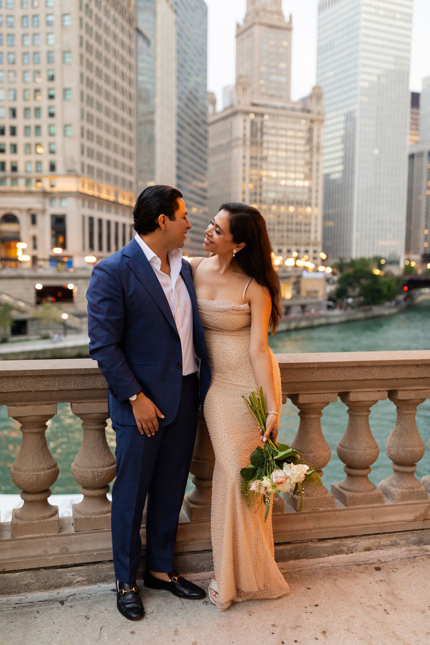 Couple in wedding attire sharing romantic moment on Chicago Riverwalk balcony with river and skyline view.