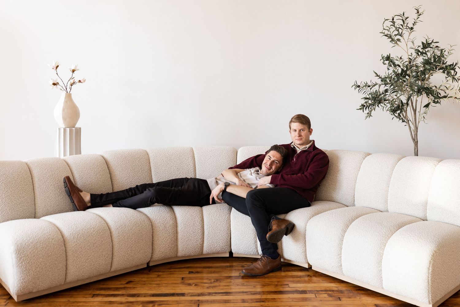 Relaxed couple lounging on curved cream sectional sofa in bright minimalist living room with wood floors.