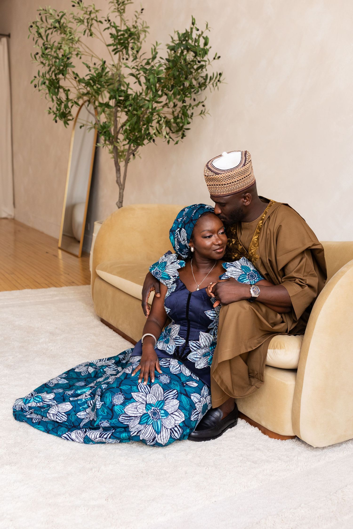 A couple in traditional Nigerian attire share an intimate moment together on a cream sofa indoors.