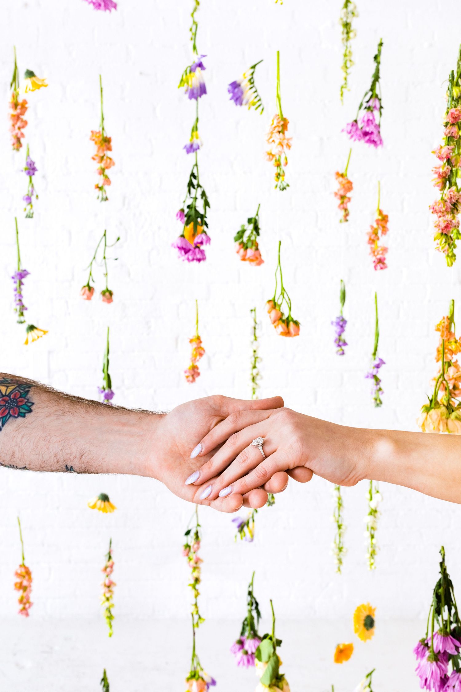 Close-up of couple holding hands with colorful hanging wildflowers in the background.