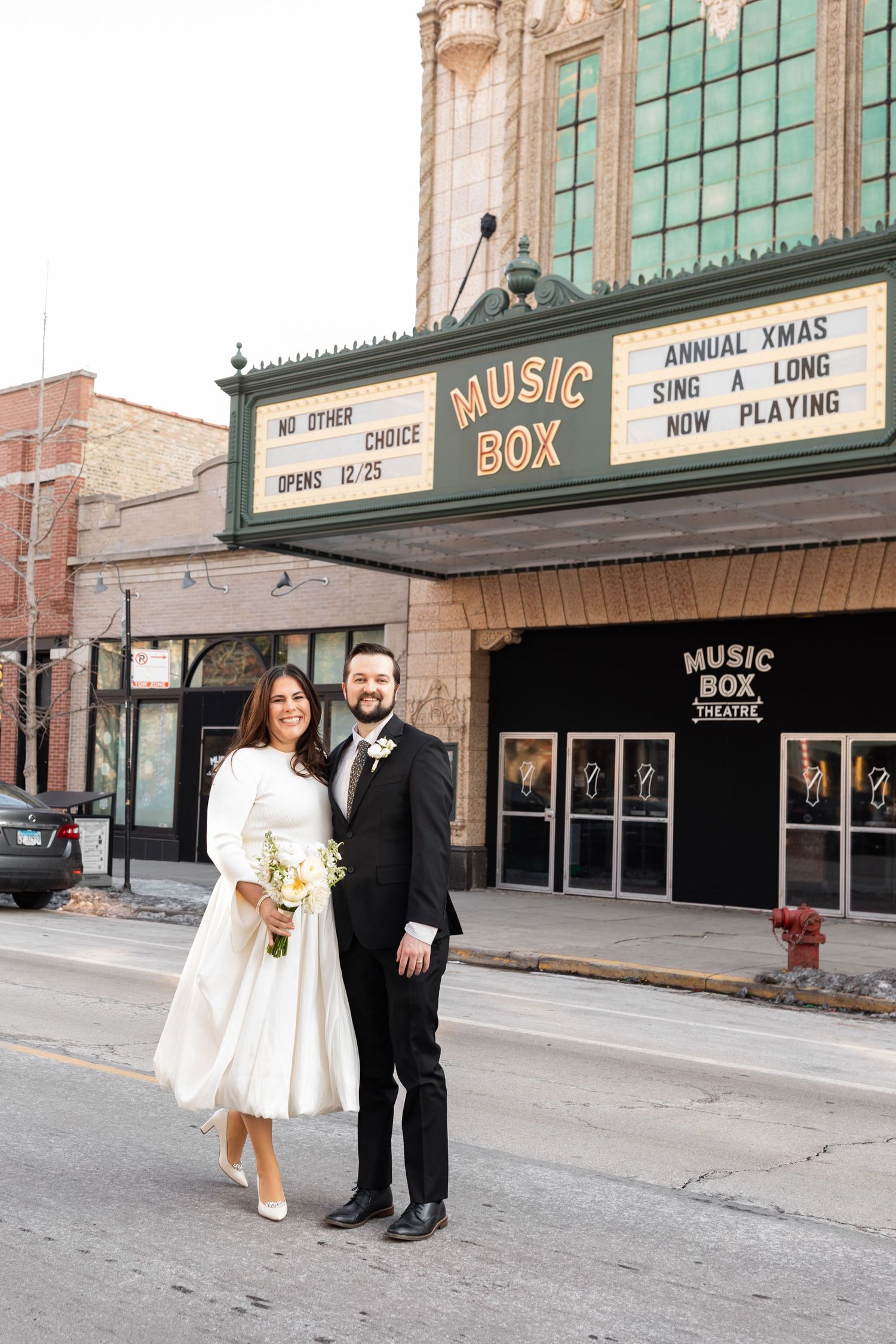 Bride and groom pose smiling in front of Chicago Music Box Theatre marquee sign.