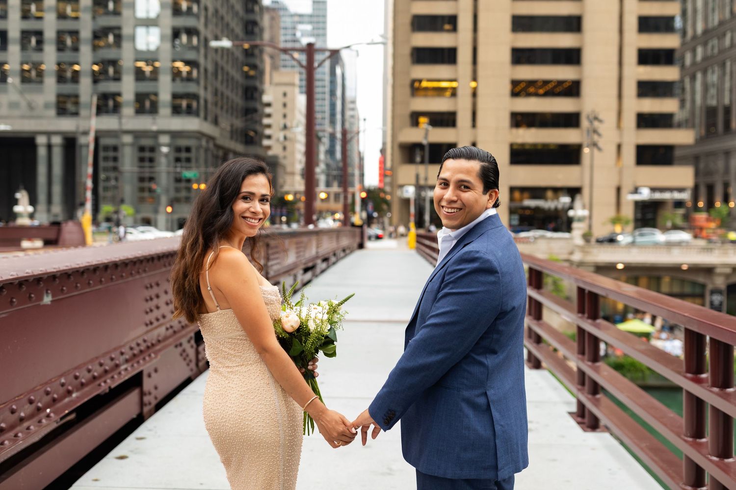 Newlywed couple holding hands on a Chicago bridge, bride in gold dress holding white bouquet.