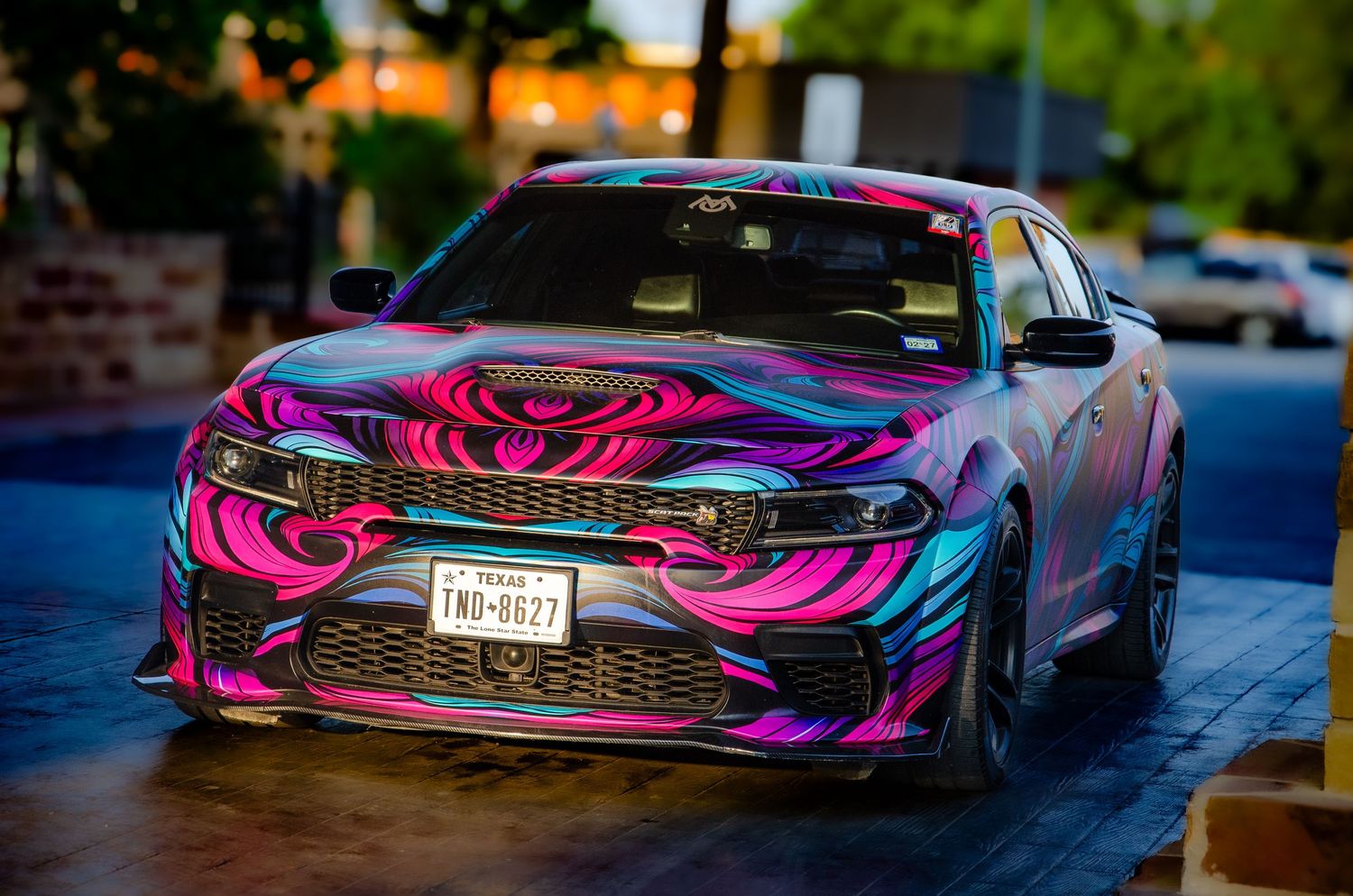Colorful psychedelic vinyl wrap Dodge Charger with pink and purple swirl design parked on urban street.