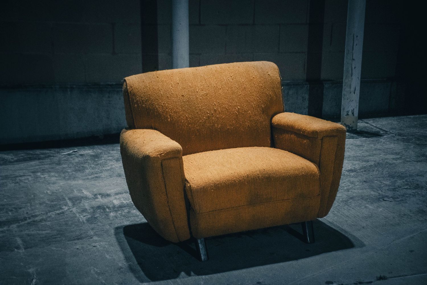 Vintage orange armchair sitting alone on a concrete floor in a dimly lit space.