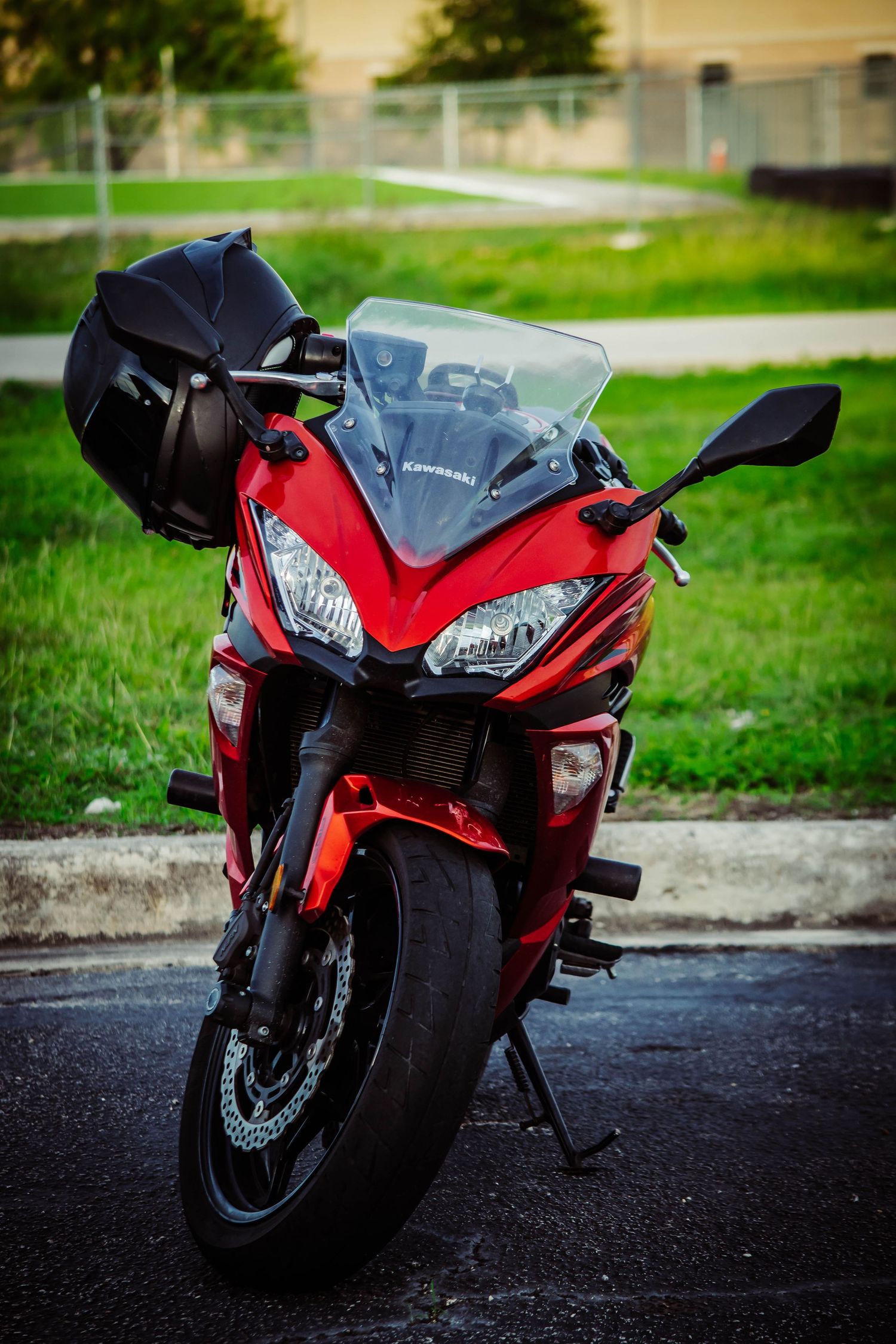 Red Kawasaki sport motorcycle parked outdoors with black helmet resting on handlebar, green grass background.