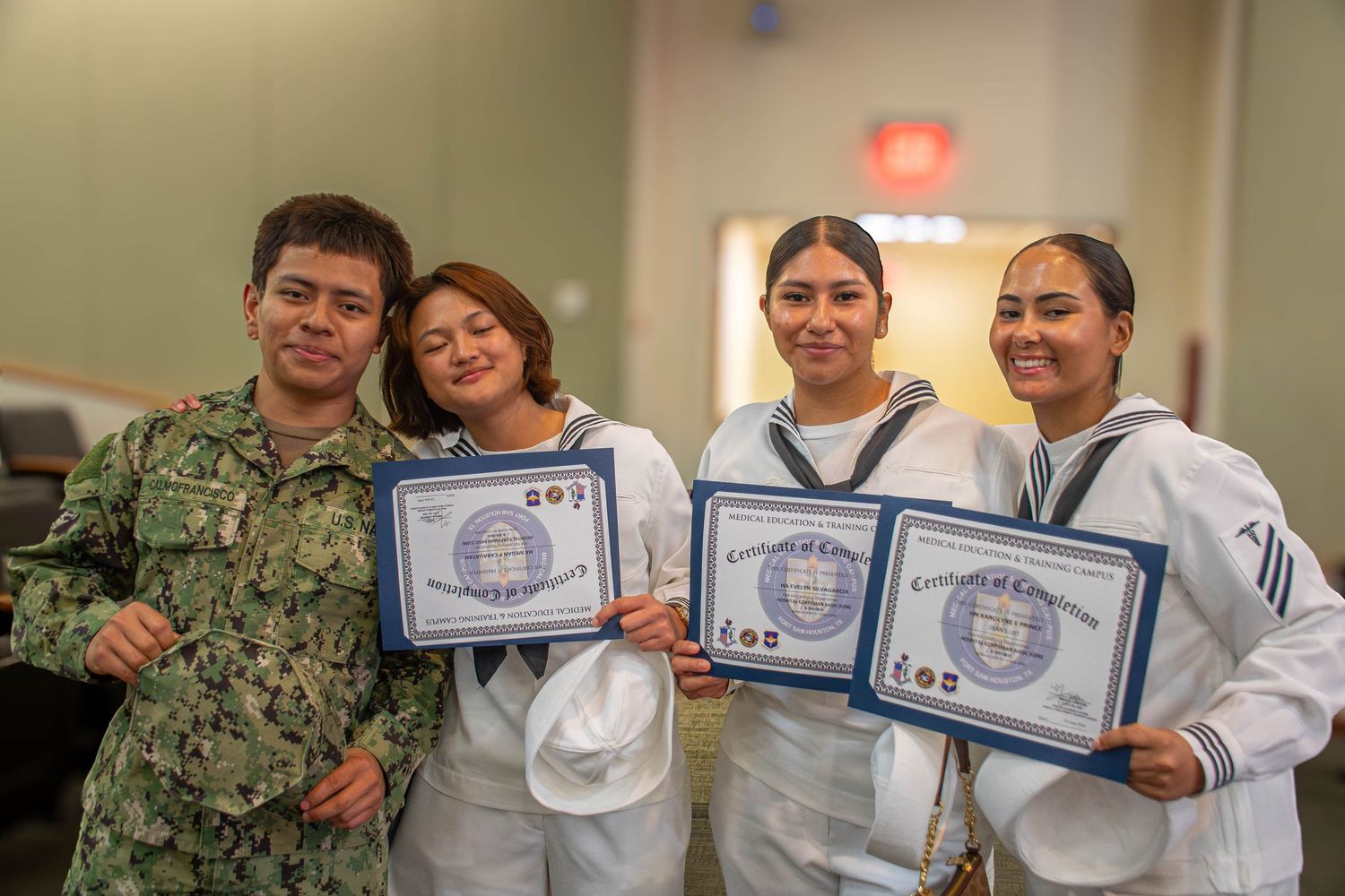 Navy sailors in white uniforms posing with certificates of achievement alongside a service member in camo.