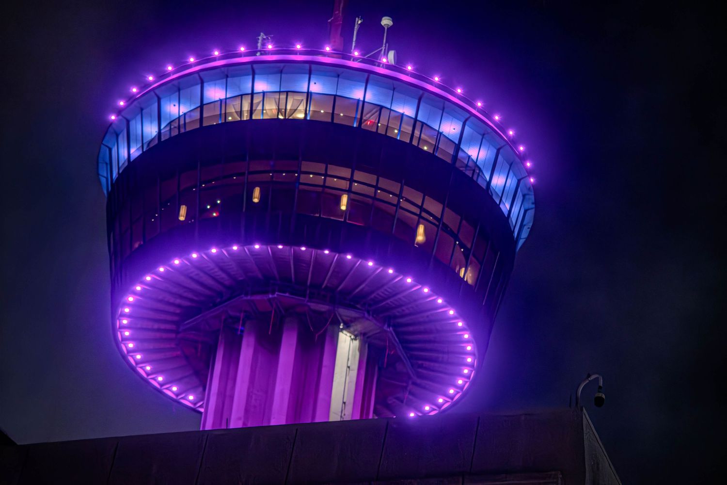 Tower of the Americas observation deck illuminated with vibrant purple LED lights against a dark night sky.