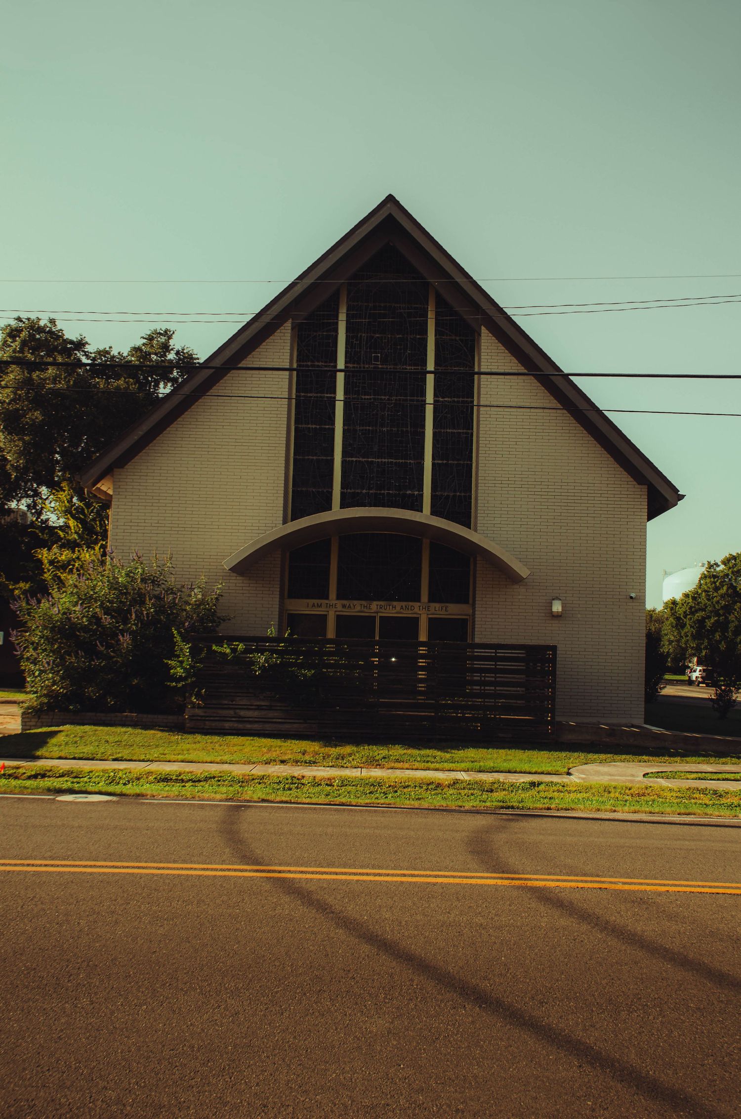Modern white church with tall A-frame facade and large windows along a quiet suburban street.