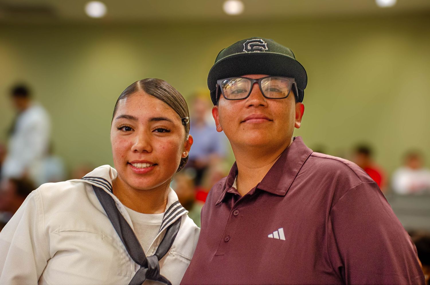Two people smiling together at a US Navy graduation ceremony event indoors.