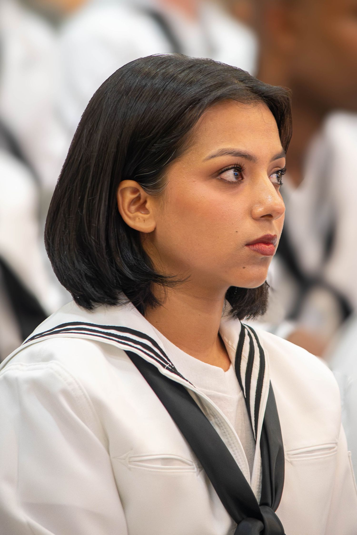 Female Navy sailor with black bob haircut in white dress uniform at military ceremony.