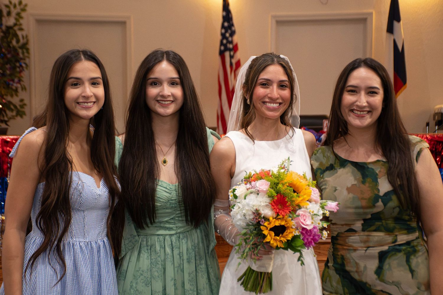 Bride in white veil holding colorful bouquet posing with three women at wedding.