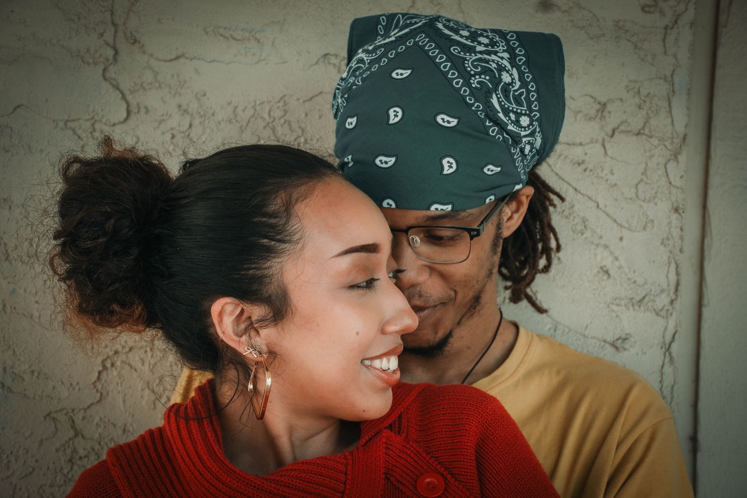A young couple sharing an intimate moment, woman smiling warmly as man wearing bandana leans close to her.