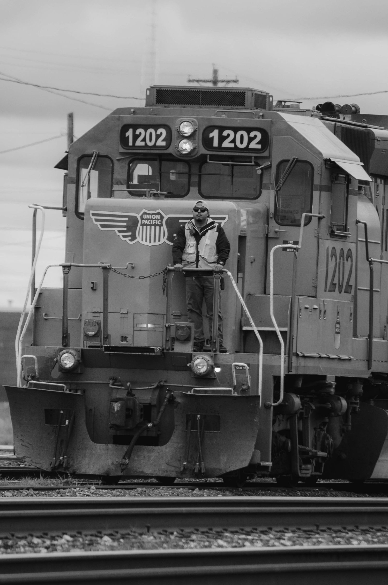 Black and white photo of a worker standing on Union Pacific locomotive 1202 on railroad tracks.
