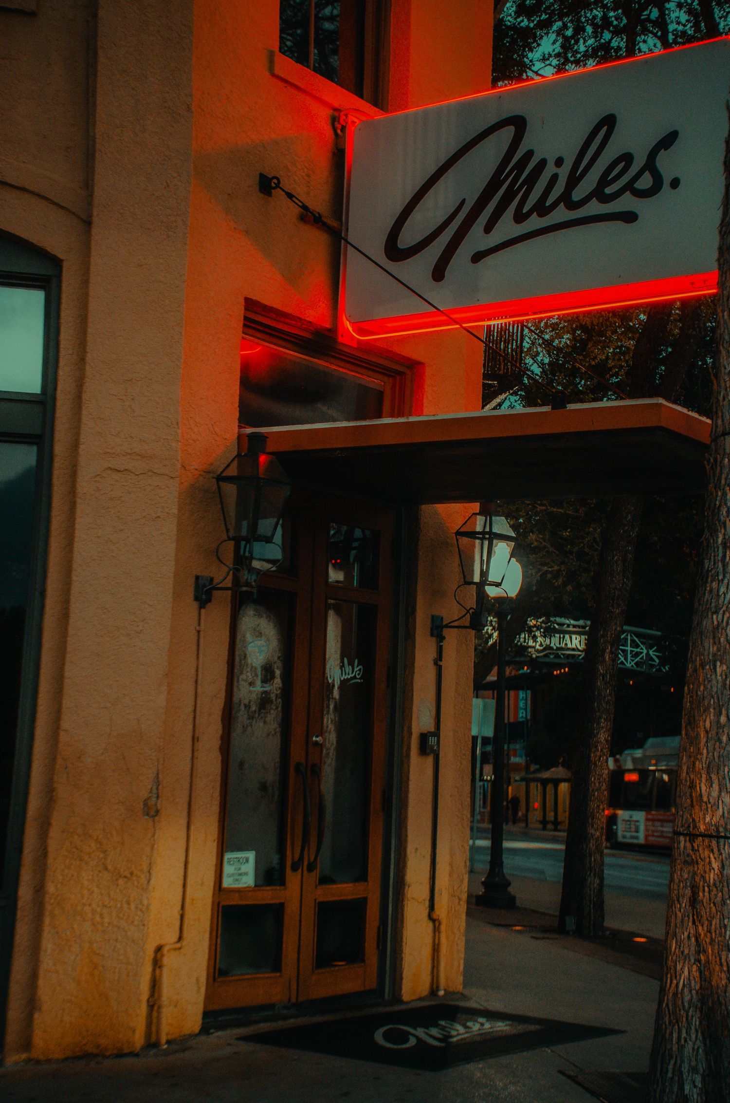 Entrance to Miles restaurant with glowing red neon sign and vintage lanterns on a city sidewalk.